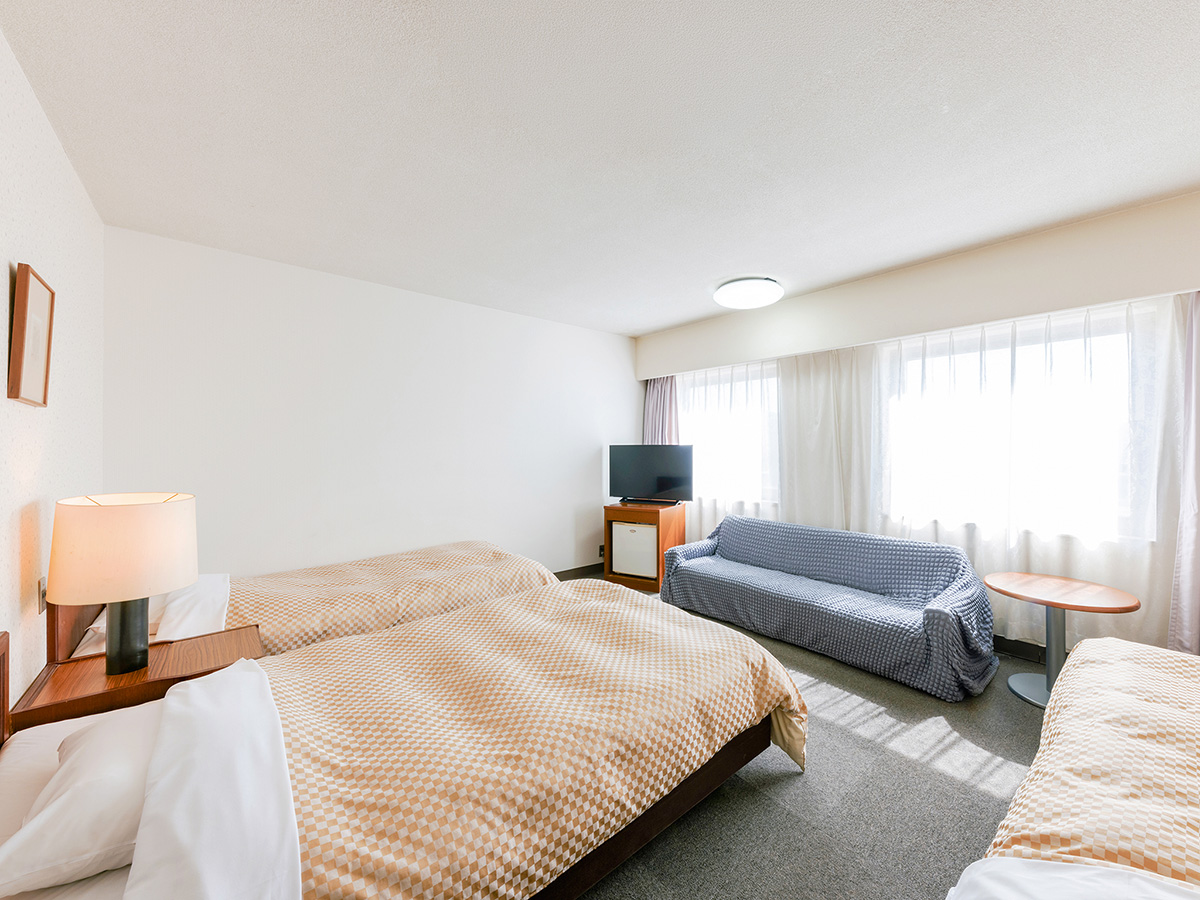 熊本県 八代グランドホテルのトリプルルーム客室。自然光が差し込む客室全体をコーナーアングルから撮影した内観