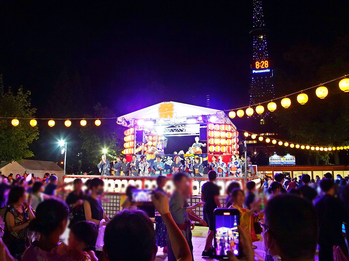 夜の大通り西2丁目で、櫓の生演奏に合わせて浴衣姿の参加者が輪になって北海盆踊りを踊る様子