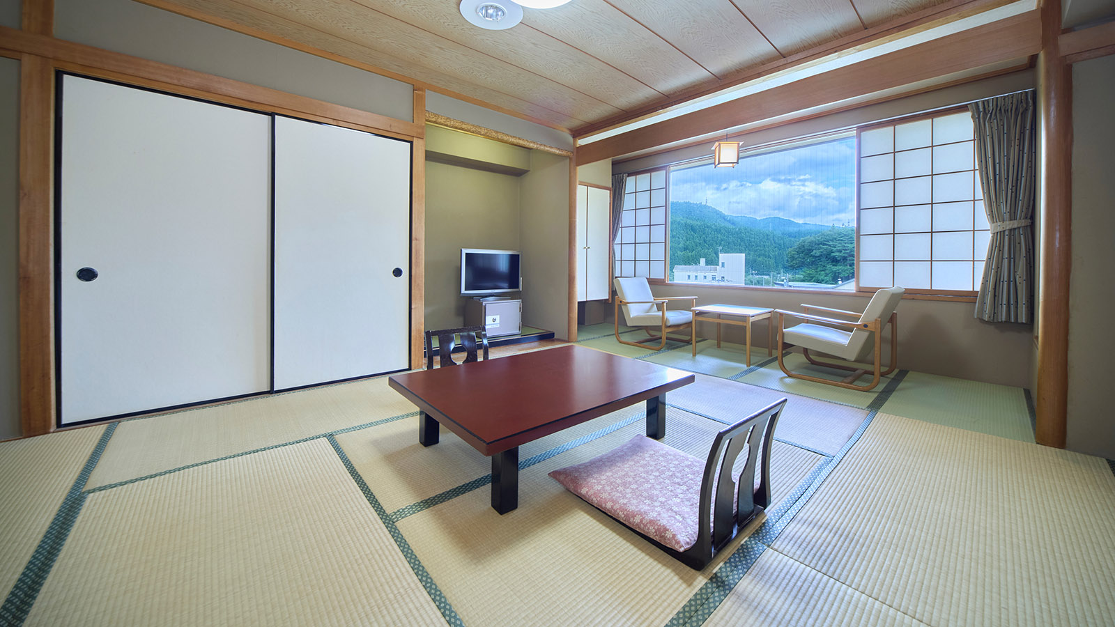 昼間の鳴子温泉ホテル亀屋の西館・和室10畳の客室。中央の座卓の奥にテレビと押し入れがあり、右側に広縁がある