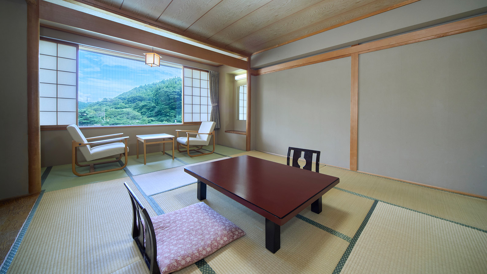 別のアングルから見た、鳴子温泉ホテル亀屋の西館・和室10畳の客室。開けられた障子窓の向こうに深緑の山と青空の景色が広がり、手前に座卓と座椅子がある